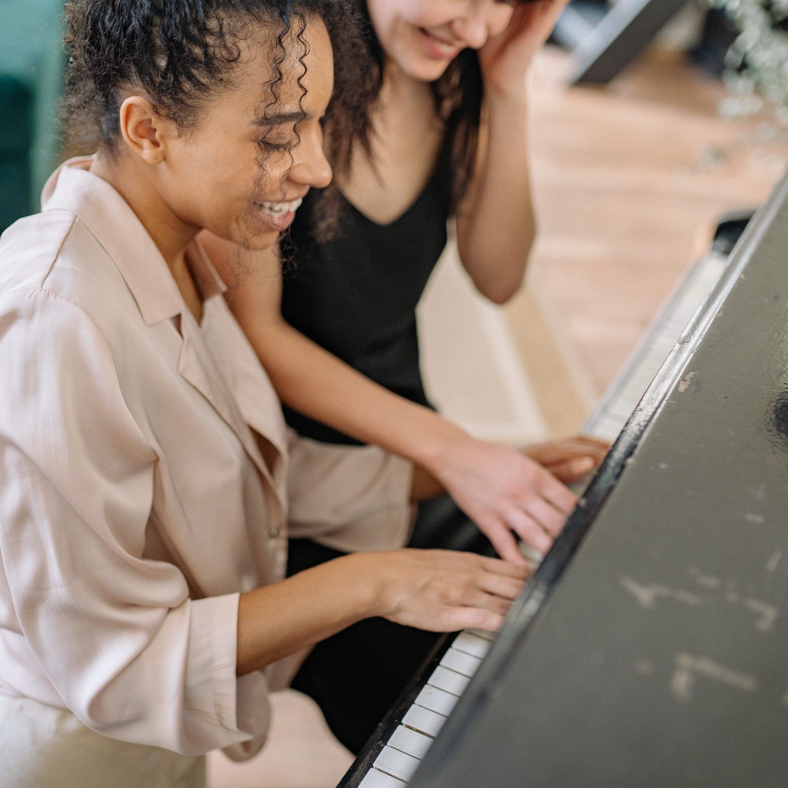 Two college student young women playing piano together and smiling