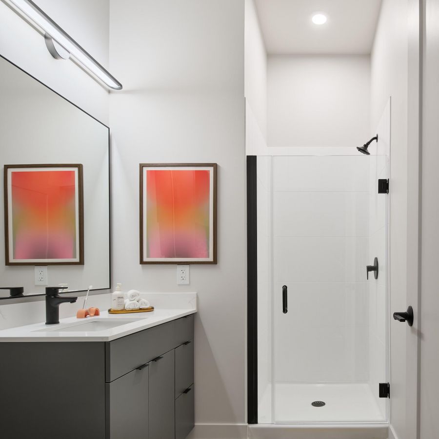 Un cuarto de baño moderno en West Lafayette con una ducha acristalada, un mueble de baño negro, obras de arte abstracto de colores vivos y una alfombra colorida sobre el suelo de madera.