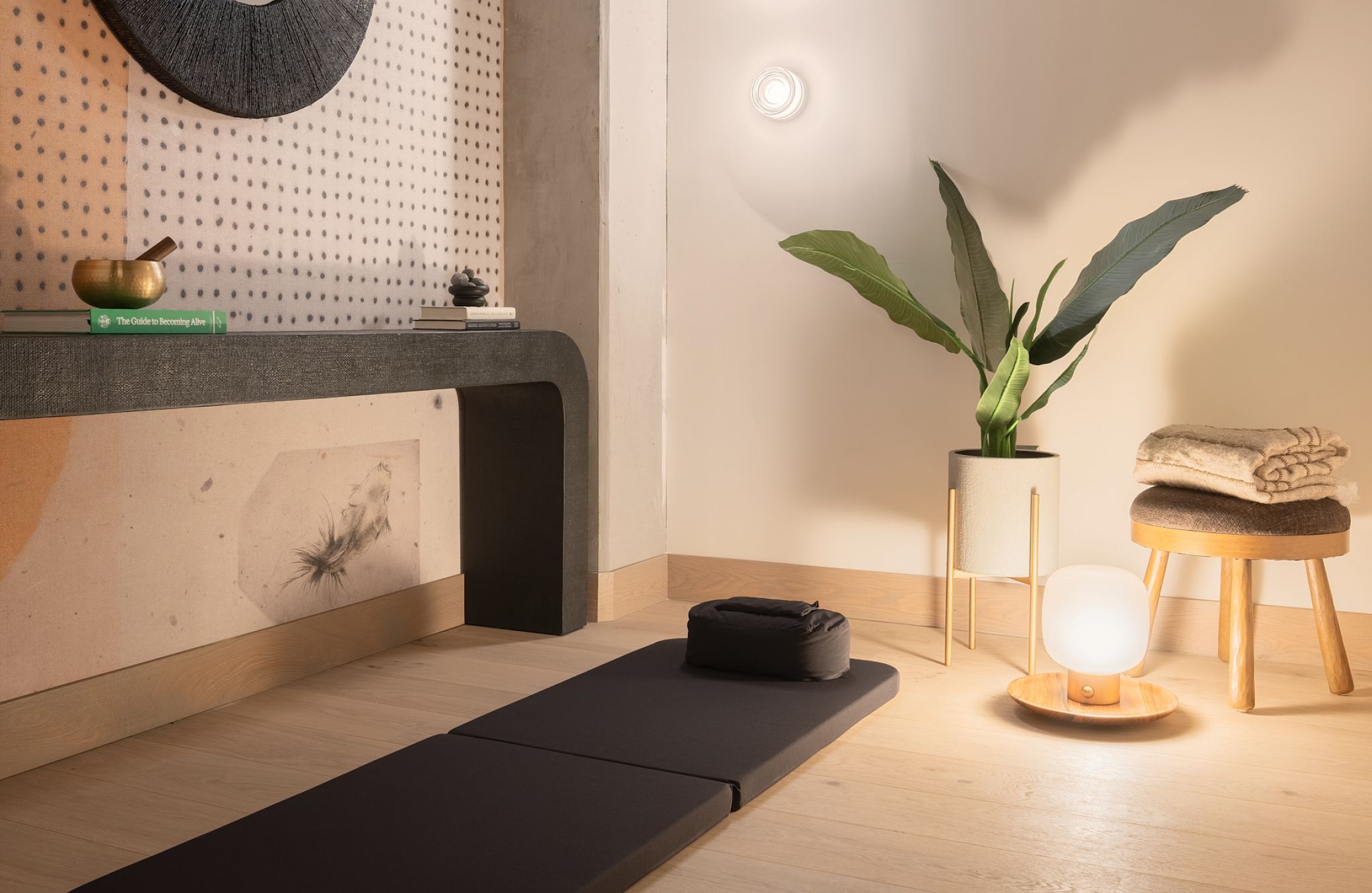 Sala de meditación moderna con una esterilla, una planta en maceta, toallas dobladas y una suave iluminación en la pared.