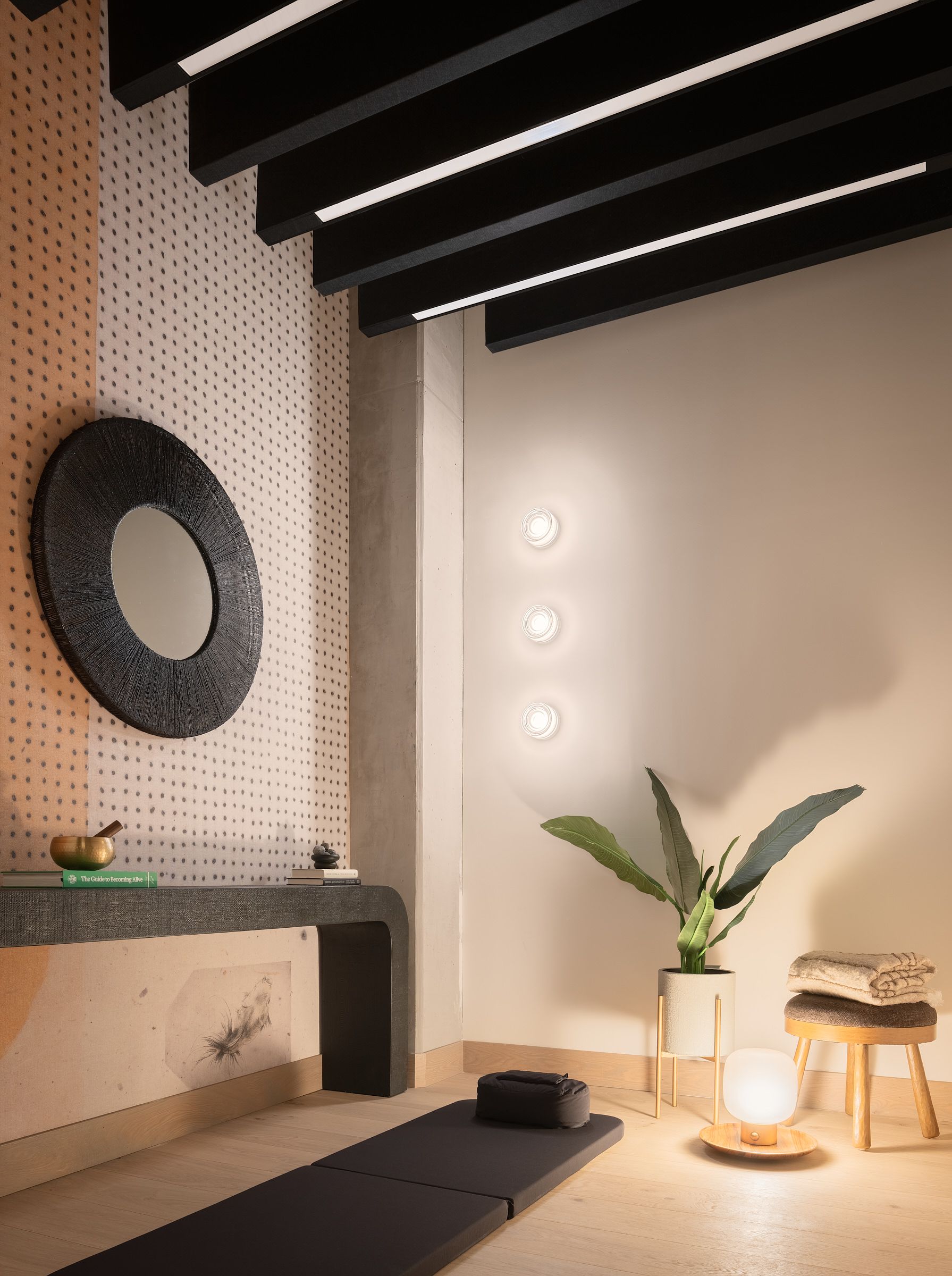 Modern meditation room with a floor mat, potted plant, folded towels, and soft lighting on the wall.