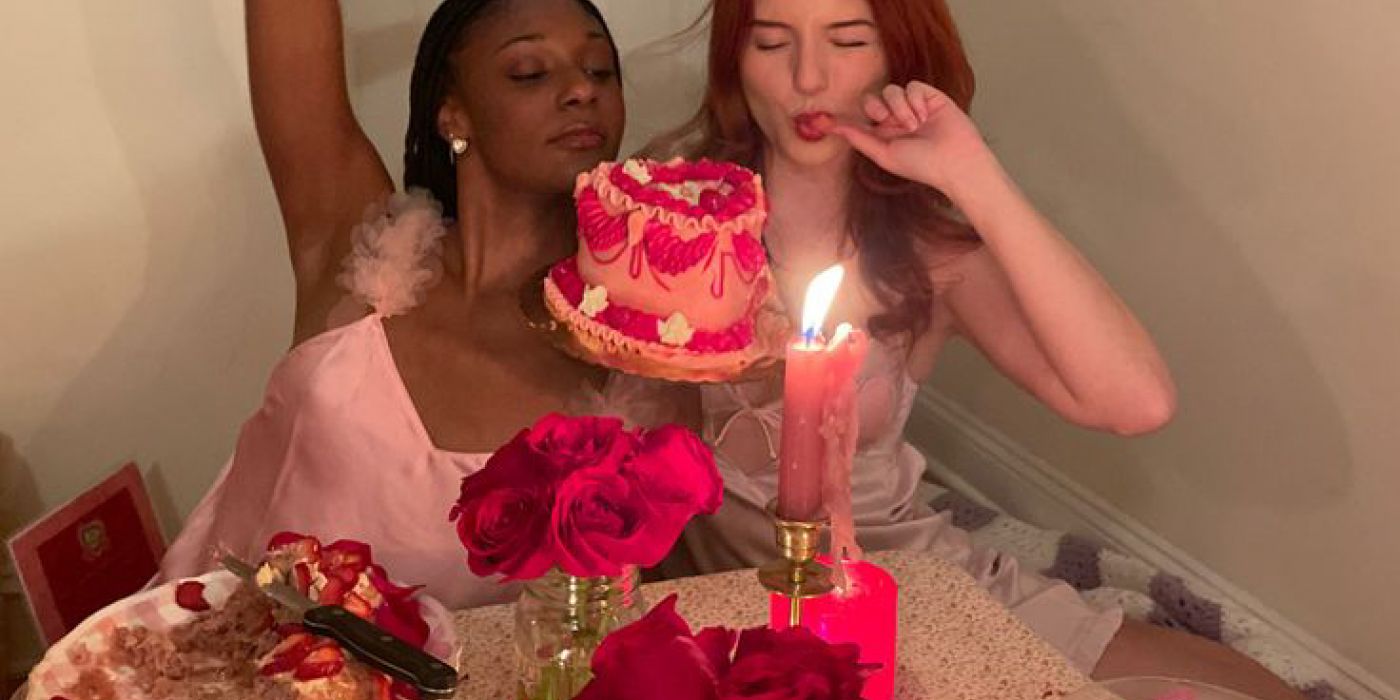 Two women in pink dresses at a decorated table with a cake, roses, and candles, giving playful expressions this February in West Lafayette.