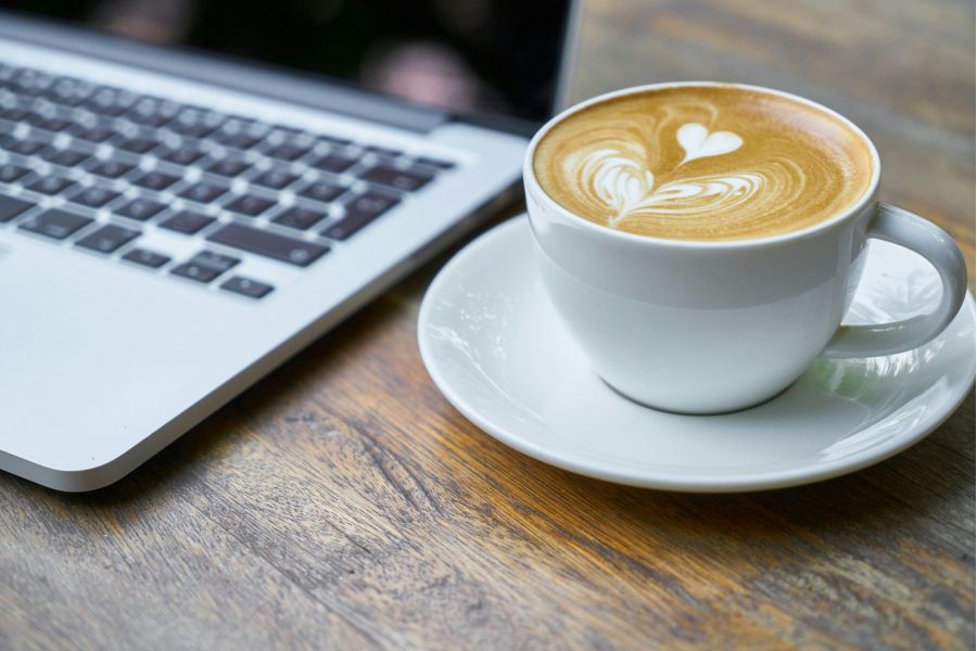 A cup and saucer filled with a latte next to a laptop