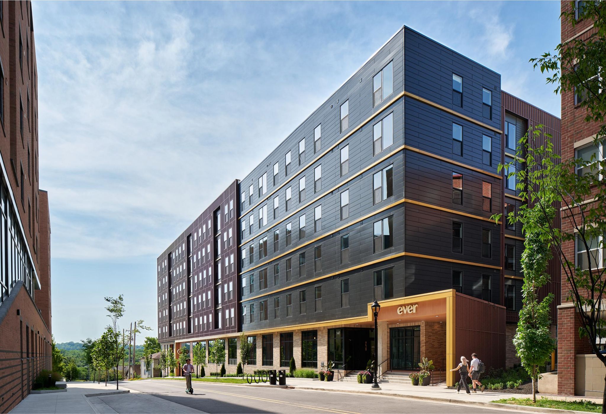 Ever West Lafayette modern mid-rise apartment building with dark panel exterior and large windows, trees along the sidewalk.