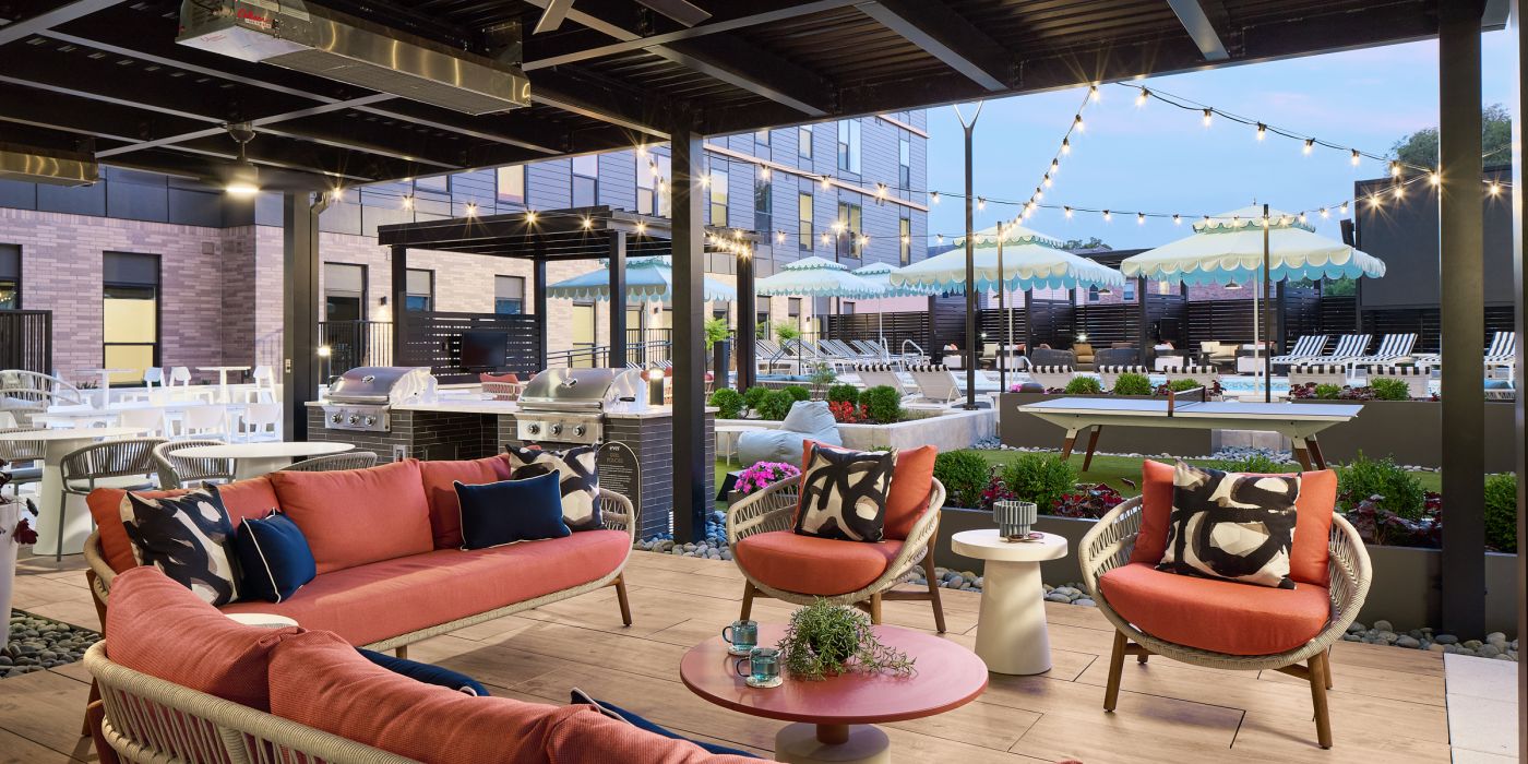 Outdoor patio with pink seating, string lights, and pool area with striped umbrellas in the background.