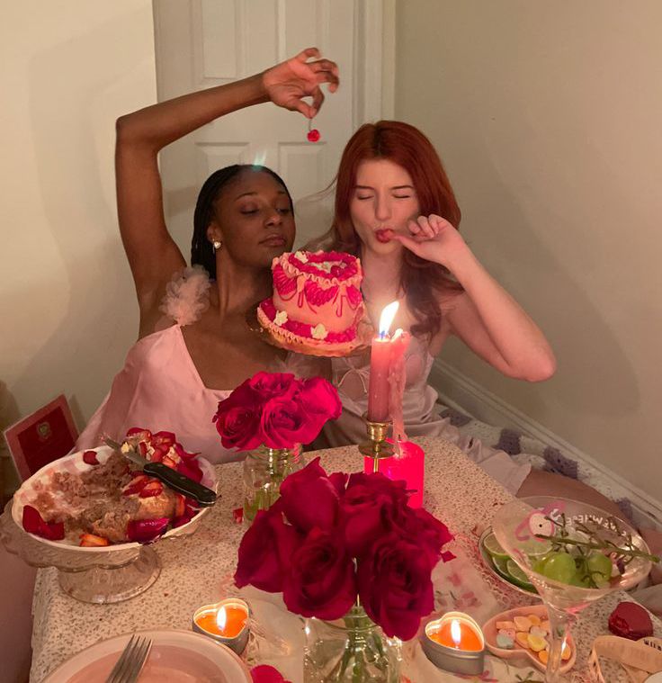 西拉法叶市二月街景：身着粉色连衣裙的两位女子坐在装饰精美的餐桌旁，桌上摆放着蛋糕、玫瑰与蜡烛，她们神情俏皮。