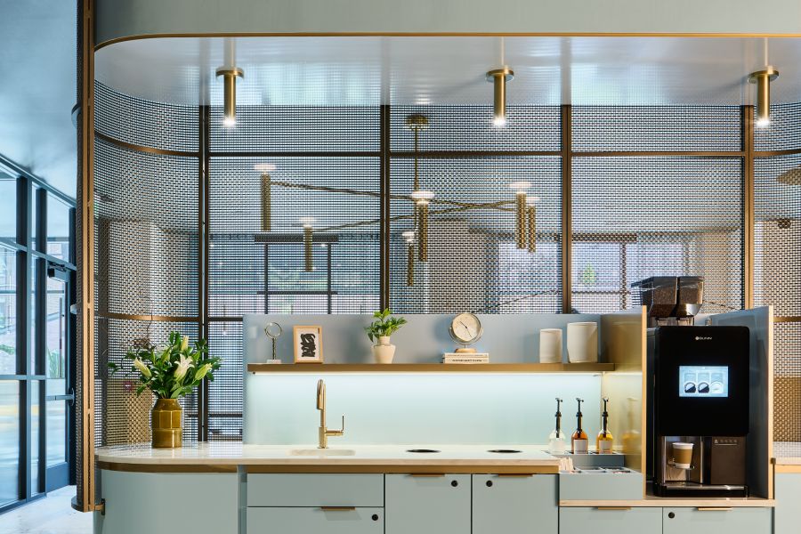Moderna estación de café con armarios azul claro, cafetera y plantas decorativas en un elegante espacio abierto.