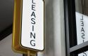 A vertical illuminated sign with the word "LEASING" mounted on a wall indoors.