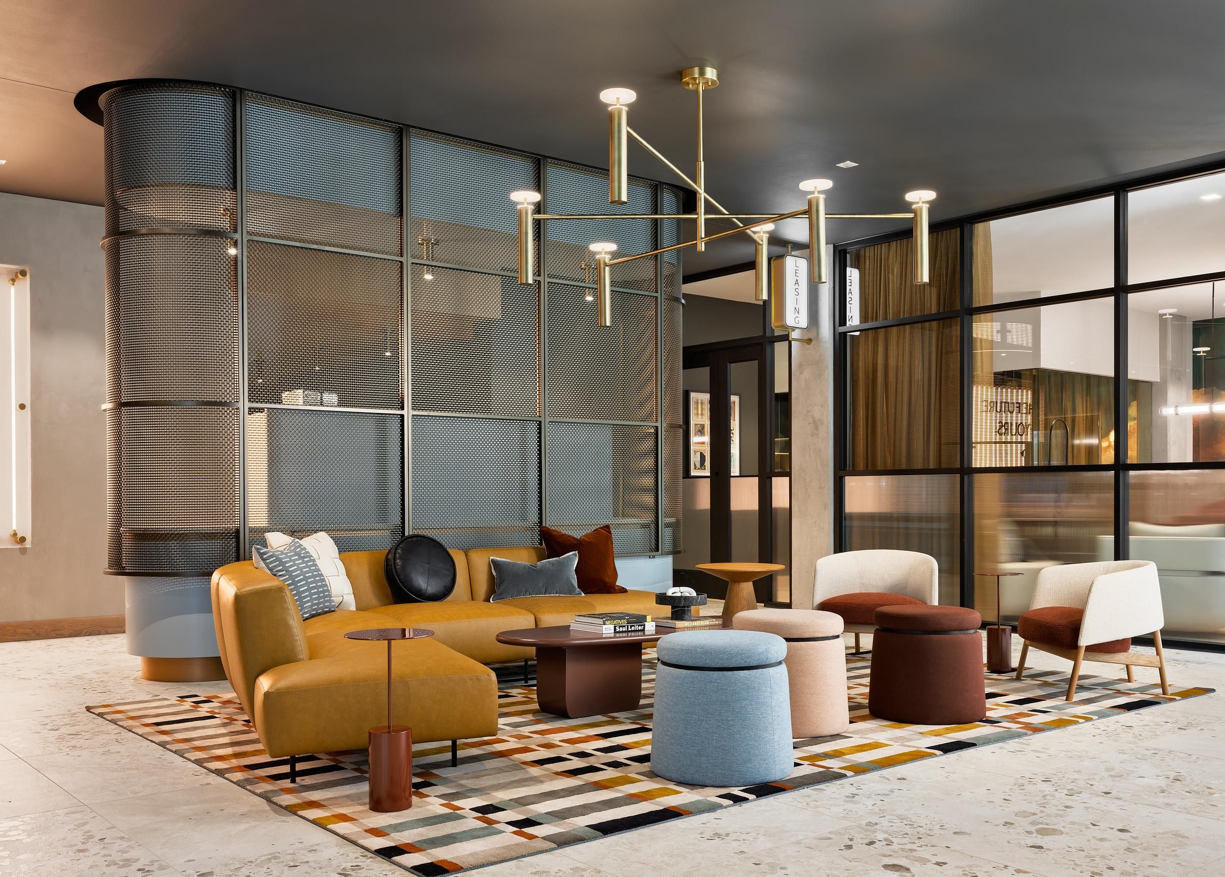 Ever West Lafayette modern lounge with colorful chairs, round tables, and geometric rug under a gold chandelier in a stylish room.