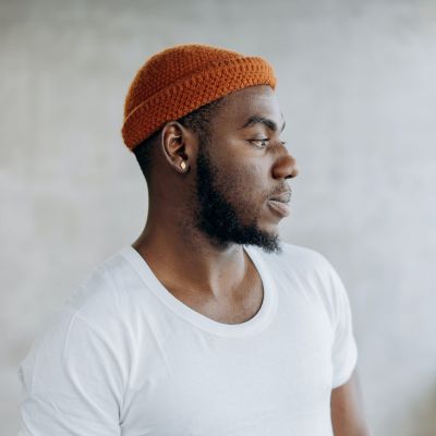 Young black man wearing an orange beanie and white shirt and looking to the side in modern aesthetic
